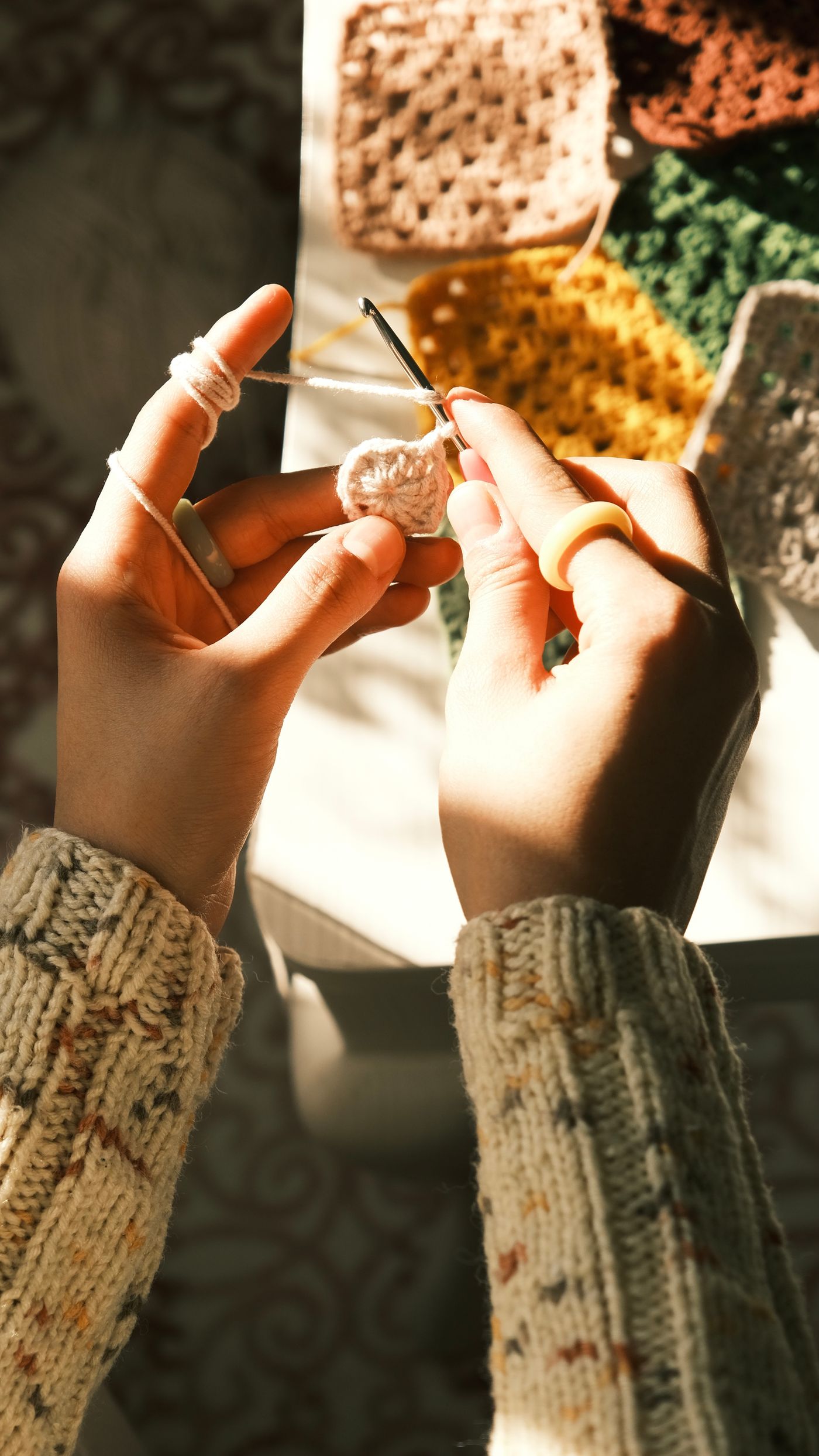 Hände beginnen mit einer Häkelnadel eine runde Häkelarbeit, daneben liegen farbige Granny Squares