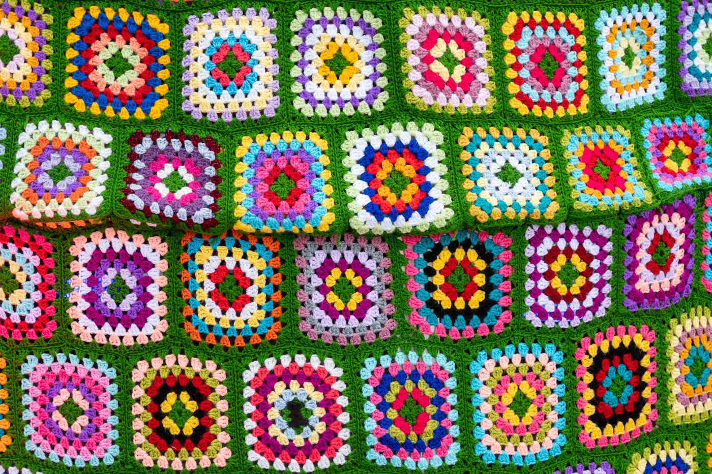 Bunte Granny Squares auf grünem Grund zu einer Decke verbunden