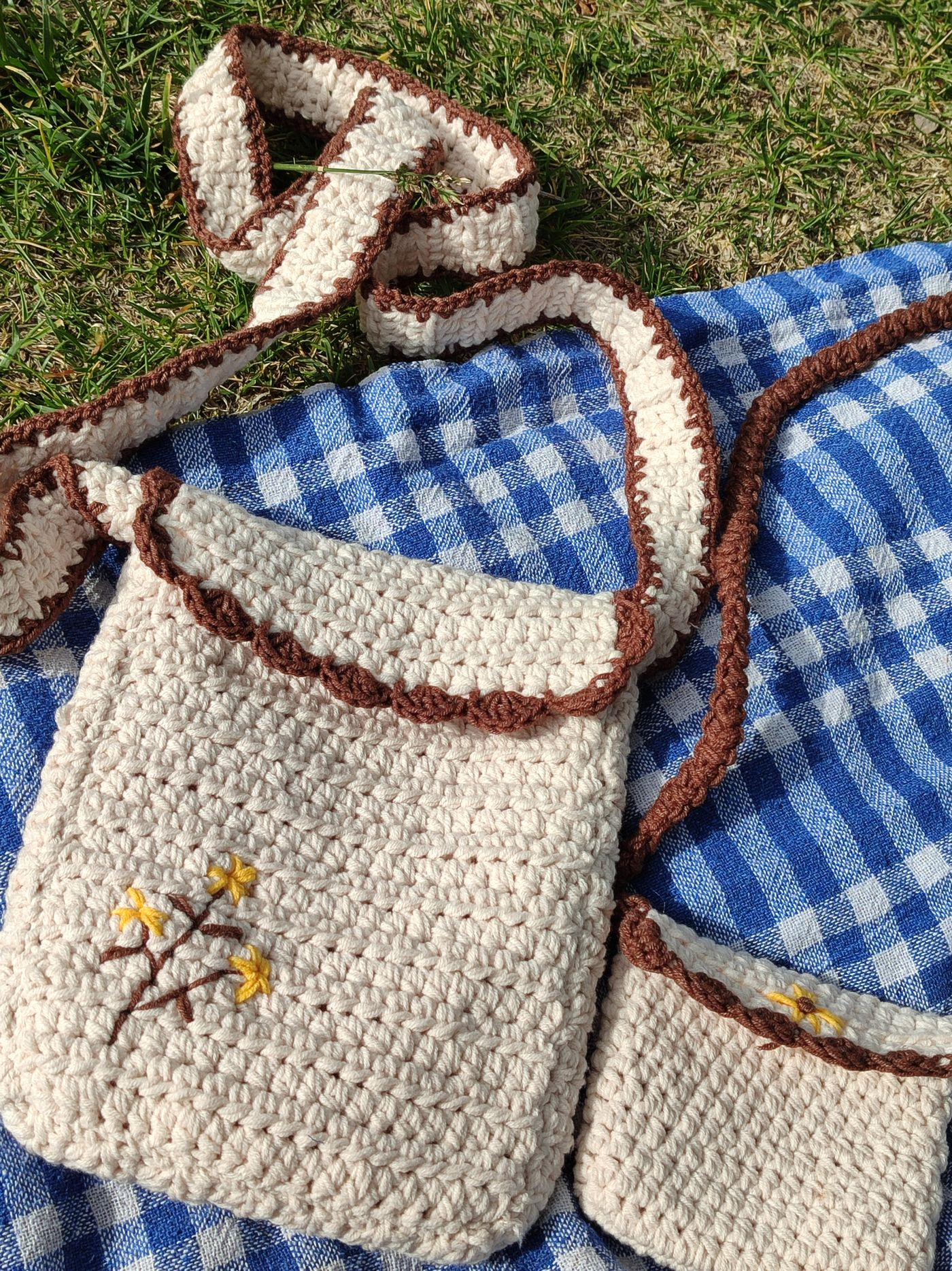 Cremefarbene gehäkelte Umhängetasche mit gesticktem Blumenmotiv auf einer karierten Picknickdecke