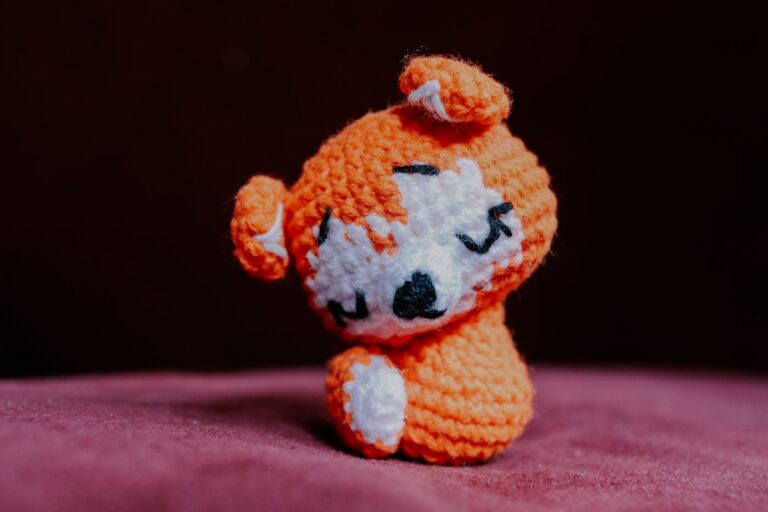 Kleine orange gehäkelte Amigurumi-Figur auf rosafarbenem Stoff