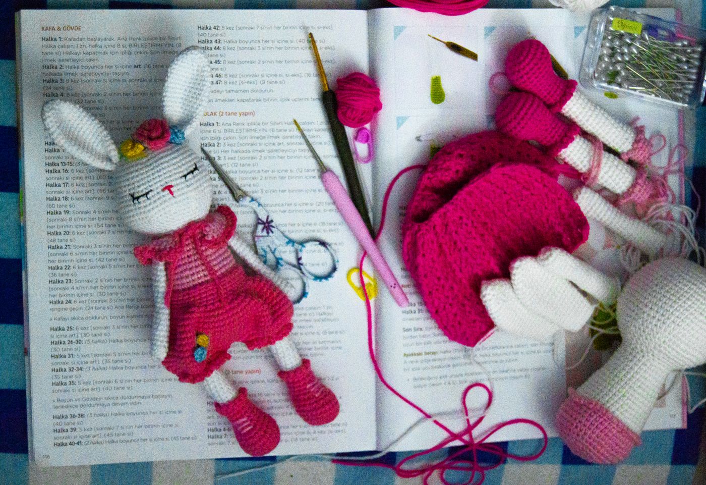 Aufgeschlagenes Häkelbuch mit einer gehäkelten Hasenpuppe, Häkelnadeln und Garn