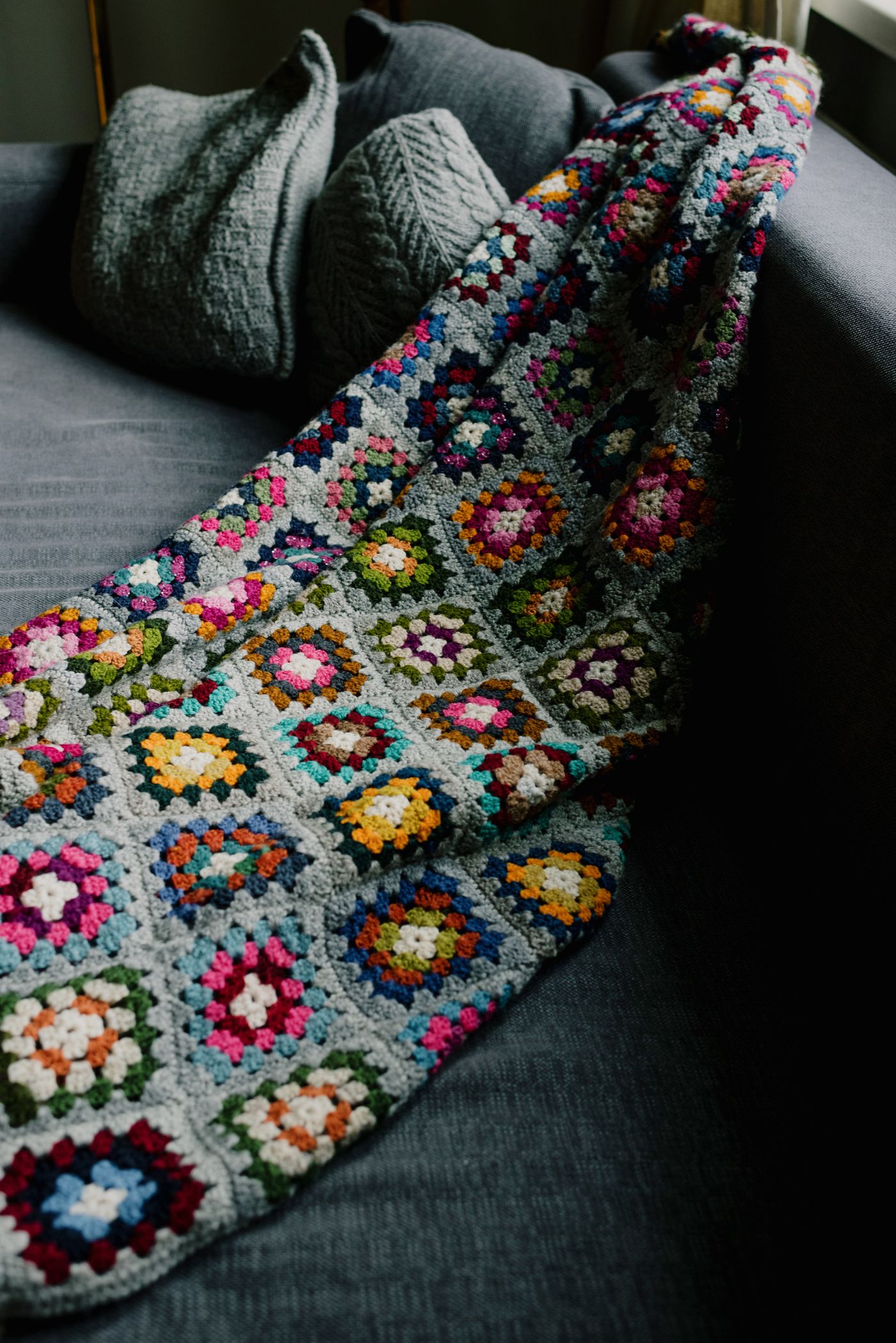 Gehäkelte Granny-Square-Decke auf einem grauen Sofa neben Kissen